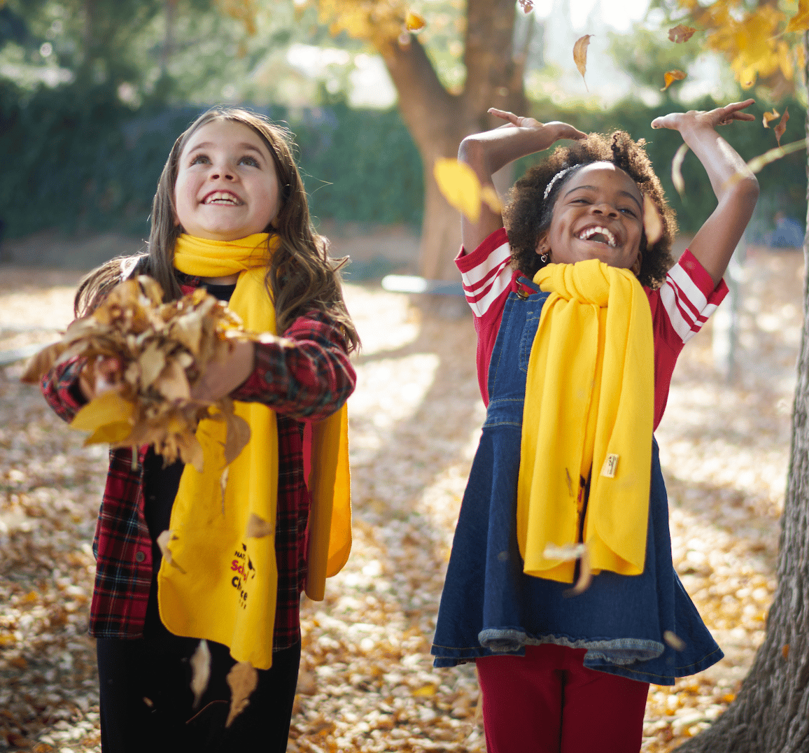 girls in yellow scarves playing in fall leaves